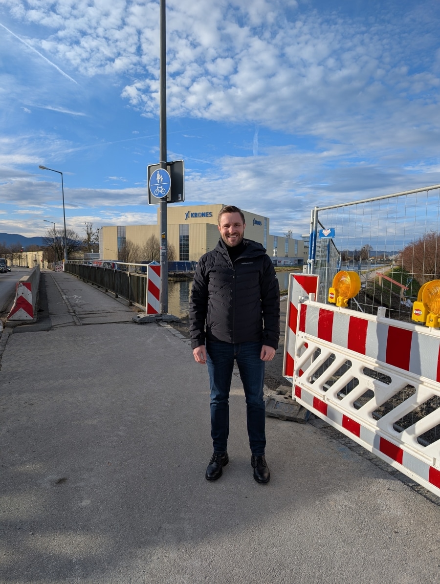 Daniel Artmann steht auf einem Gehweg neben einer Baustelle. im Hintergrund sieht man das Krones-Gebäude.